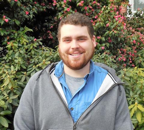 Zach smiling outside of the Old Main building in front of bushes