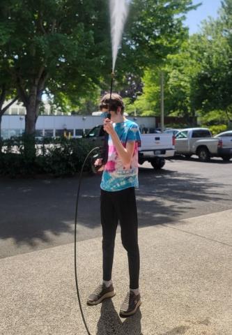 student in the parking lot on a summer day holding a hose