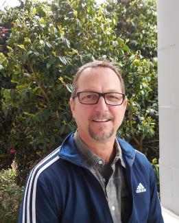 David Zilavy, a man smiling with dark hair and glasses, wearing a blue jacket standing outside of Old Main at WSSB.