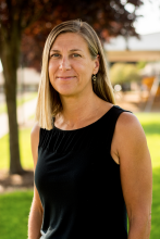 Danielle King. A smiling woman standing outdoors, shown from waist up, background is sunlit with partial view of WSSB campus.