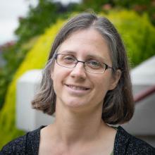 Kirsten Dlugo a woman in her early forties with gray brown hair and glasses standing in front of Old Main at WSSB campus.