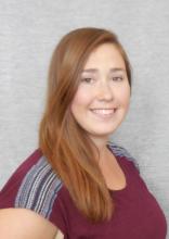 Ashley Woodruff, a young woman with long brown/red hair, wearing a maroon shirt, and smiling at the camera.